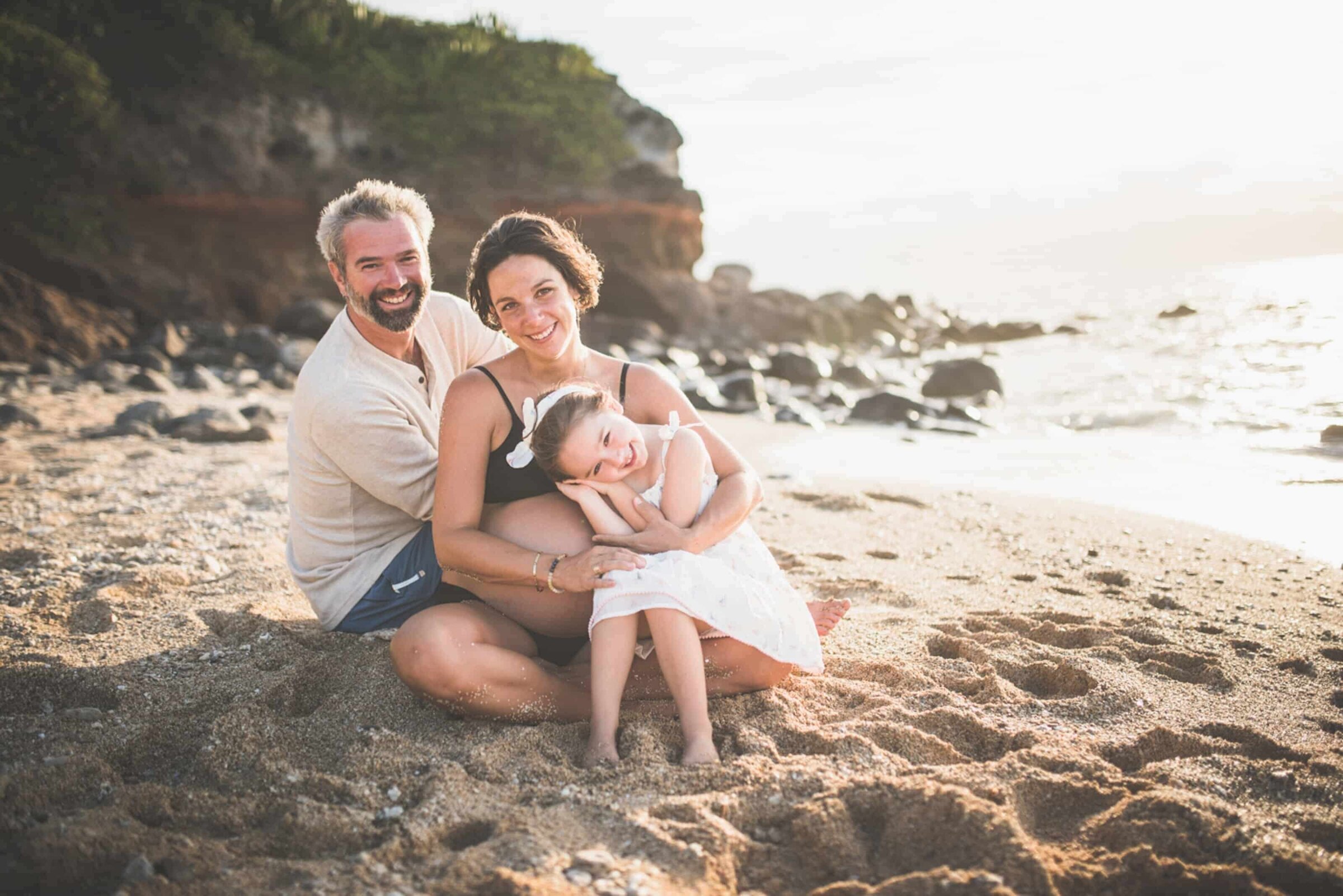 maui-family-photographer-dreamgraphy-golden-hour-beach-session Family of three sitting on a beach posing for a family photo. Mom is expecting a baby.