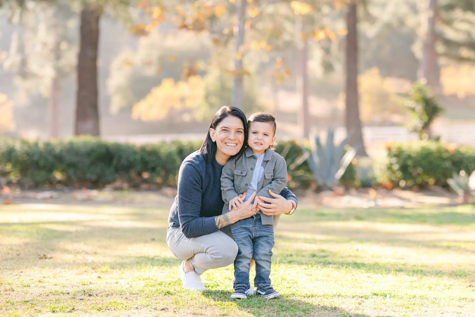 Los Angeles Photographer — Family Session at Mulholland Fountain & Griffith Park Los Angeles photographer capturing a mother crouching down smiling with her toddler son in a sunlit park at Mulholland Fountain in Griffith Park