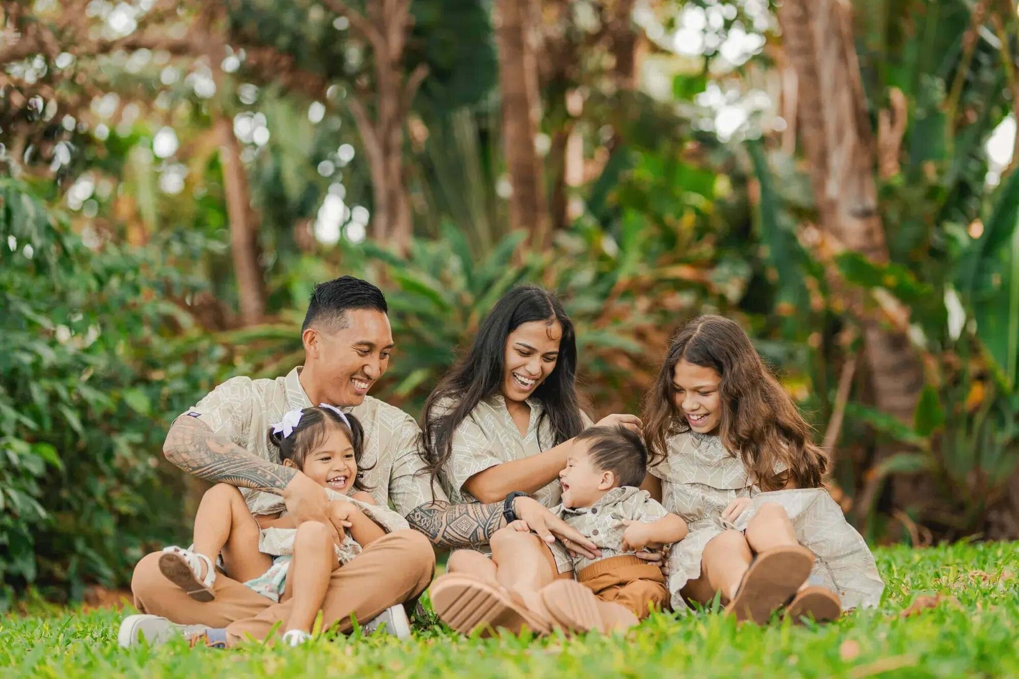 A family of five laughing together on the grass surrounded by lush tropical greenery during a candid family photography session in Maui