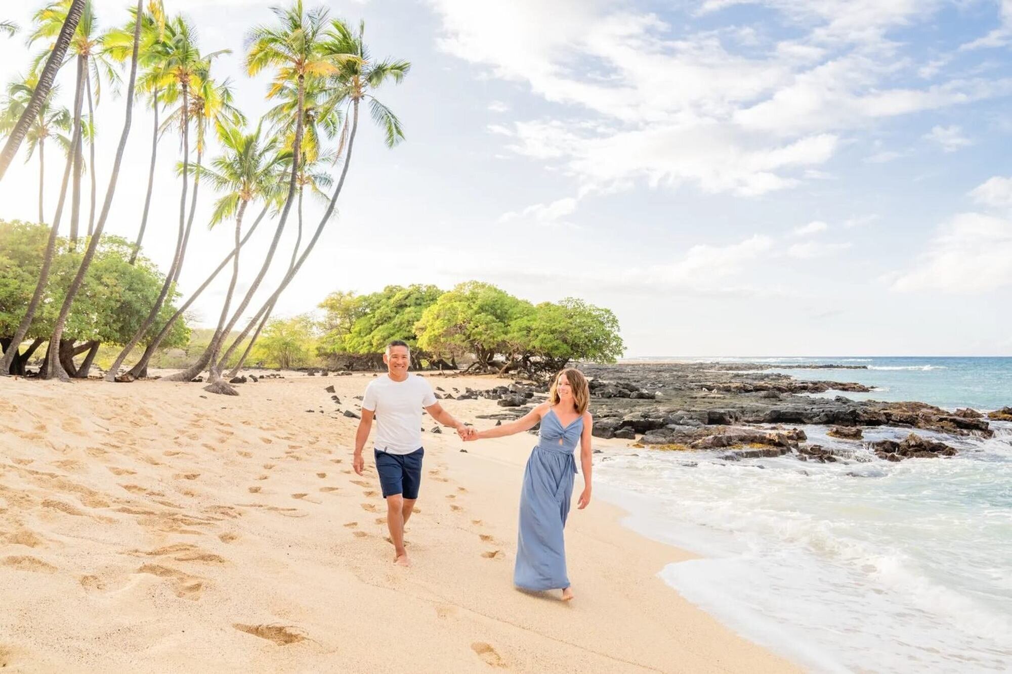 A couple walking hand in hand along a tropical beach during a romantic vacation photoshoot