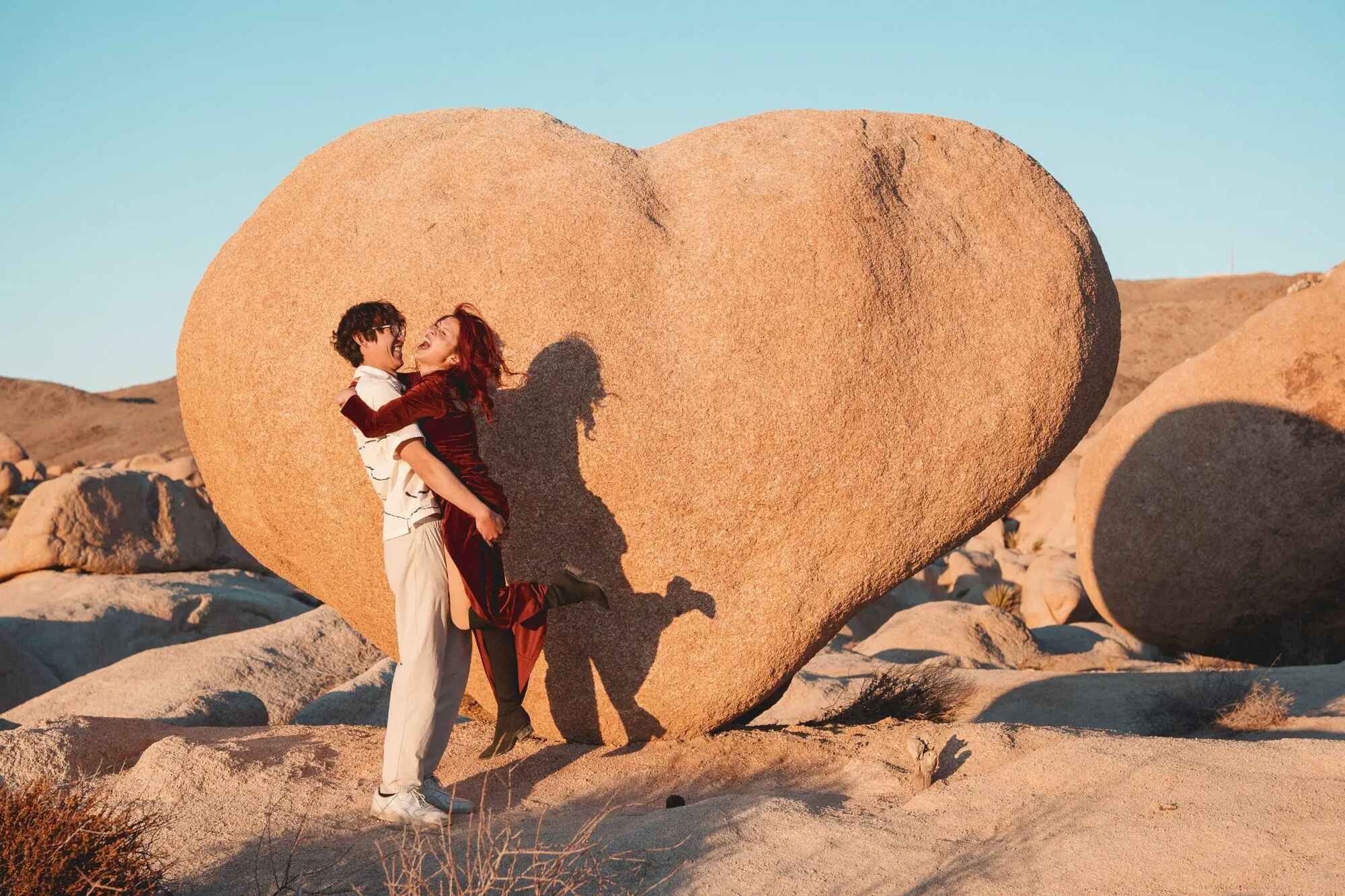 Los Angeles couples photographer capturing a couple laughing and spinning together in front of the iconic heart-shaped boulder at Joshua Tree National Park at golden hour