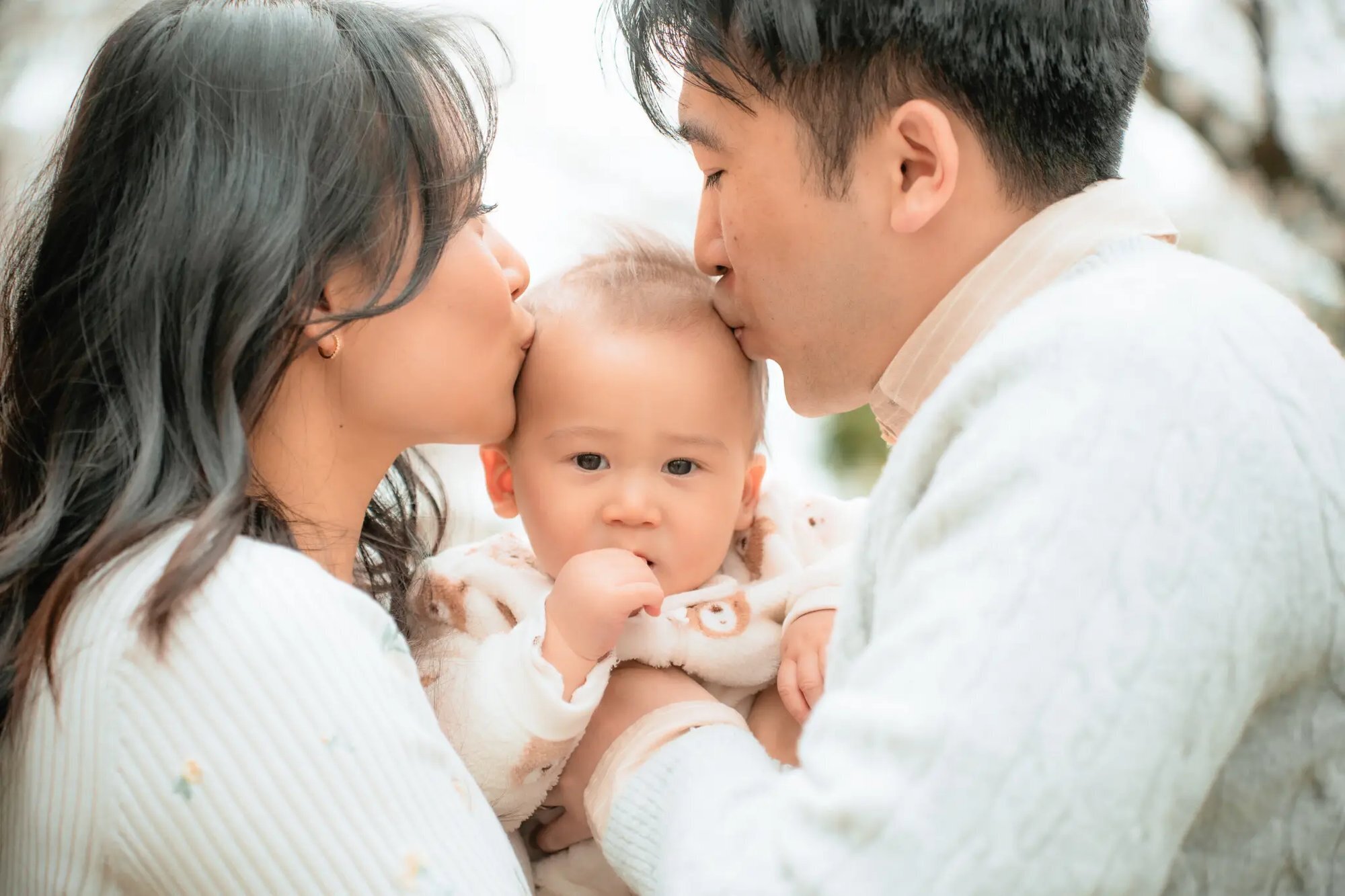 Parents kissing their baby on the cheeks during a professional family photo session in Fukuoka, Japan