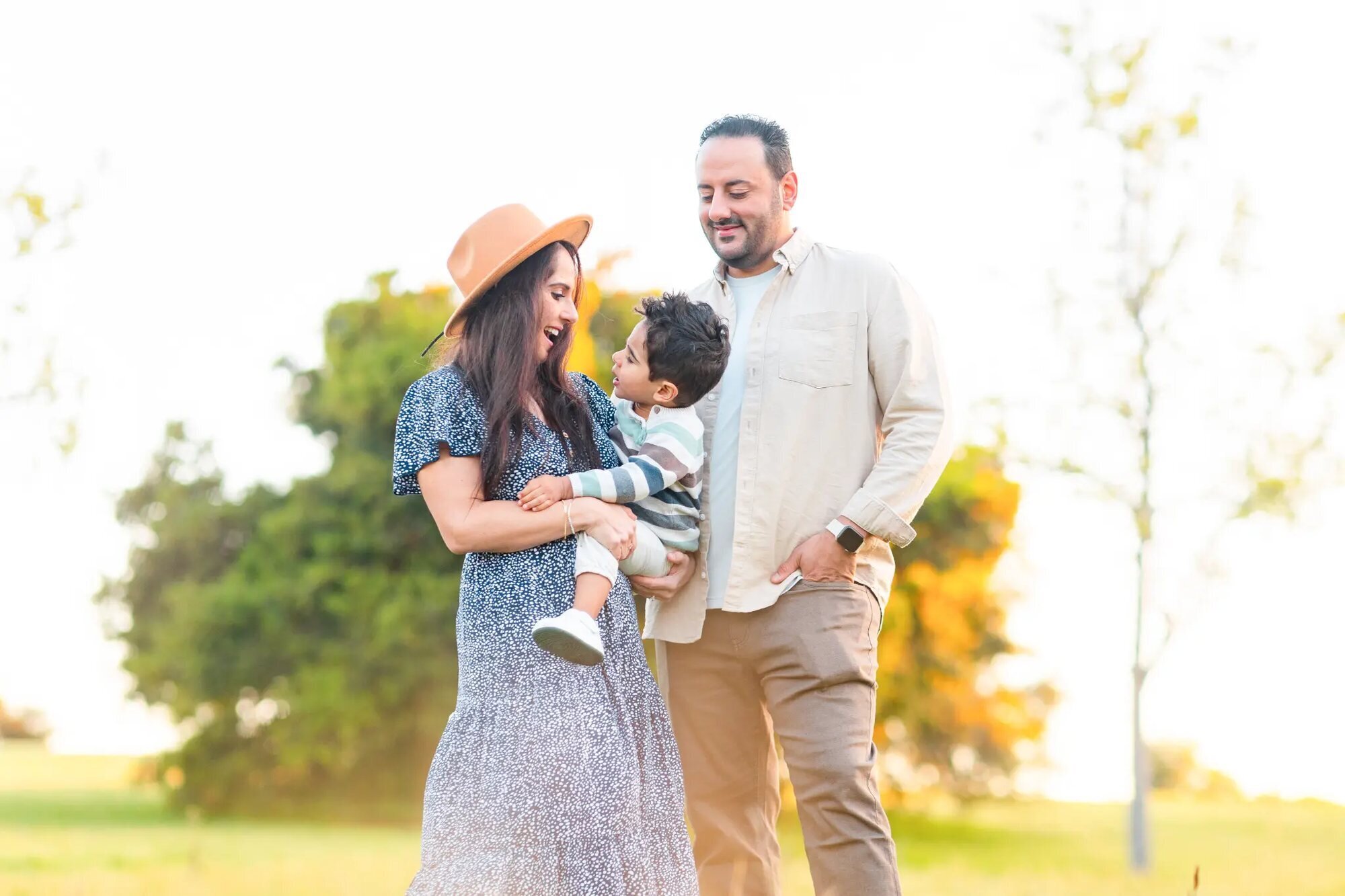 Los Angeles family photographer capturing a mother in a blue floral dress and wide-brim hat laughing with her toddler son while the father smiles beside them at Kenneth Hahn State Recreation Area