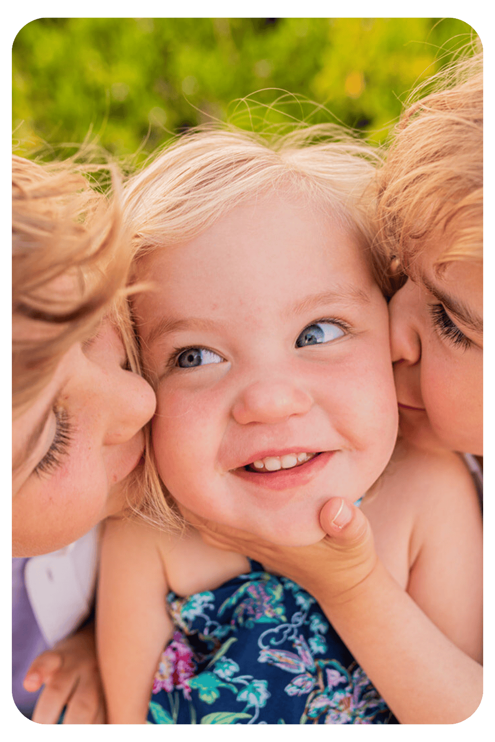 Two young siblings kissing their laughing baby sister on the cheeks during a candid outdoor family photoshoot