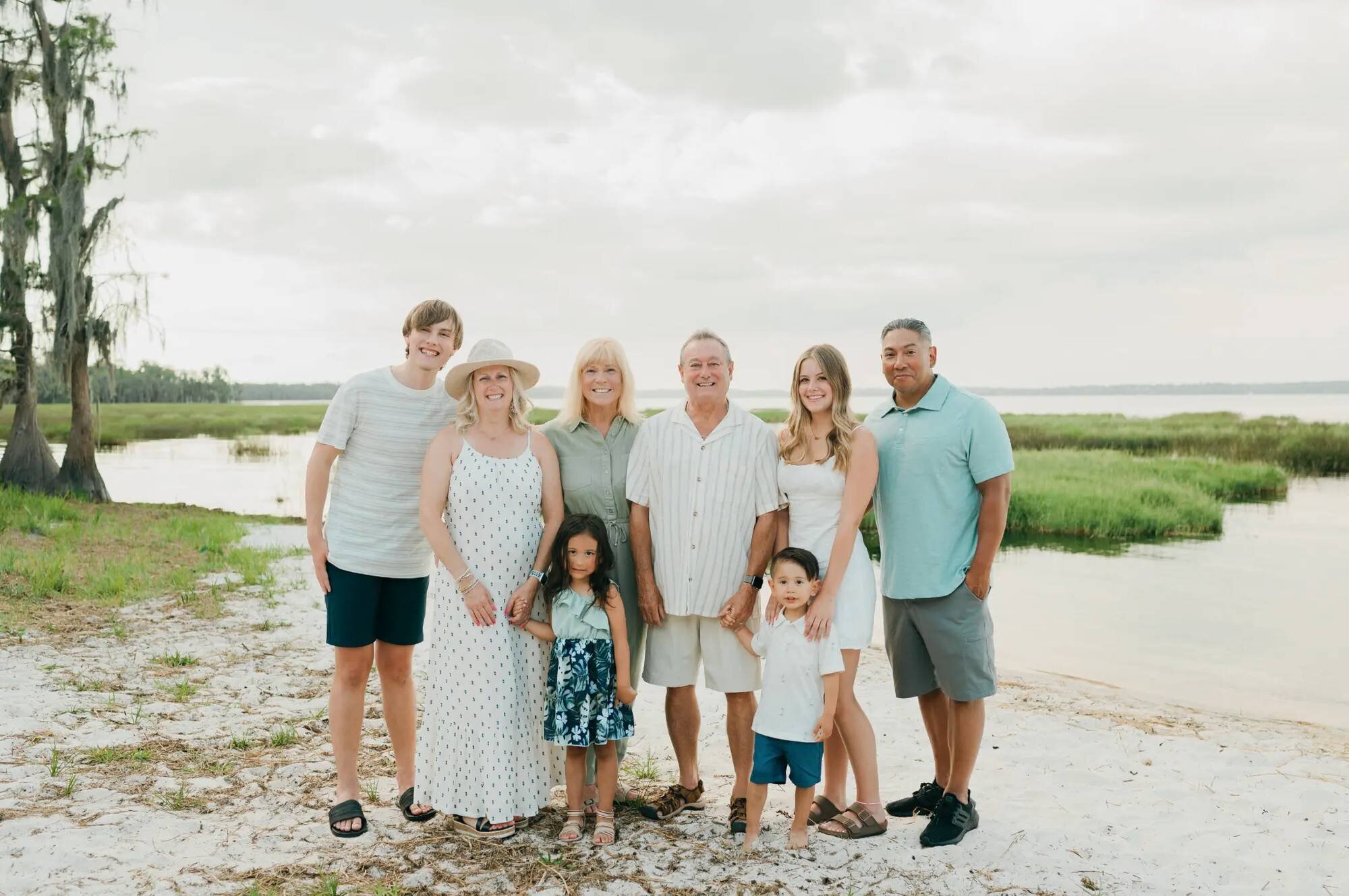 Orlando family photographer capturing a multigenerational extended family of eight smiling together at a Florida lakeside with cypress trees and marshland