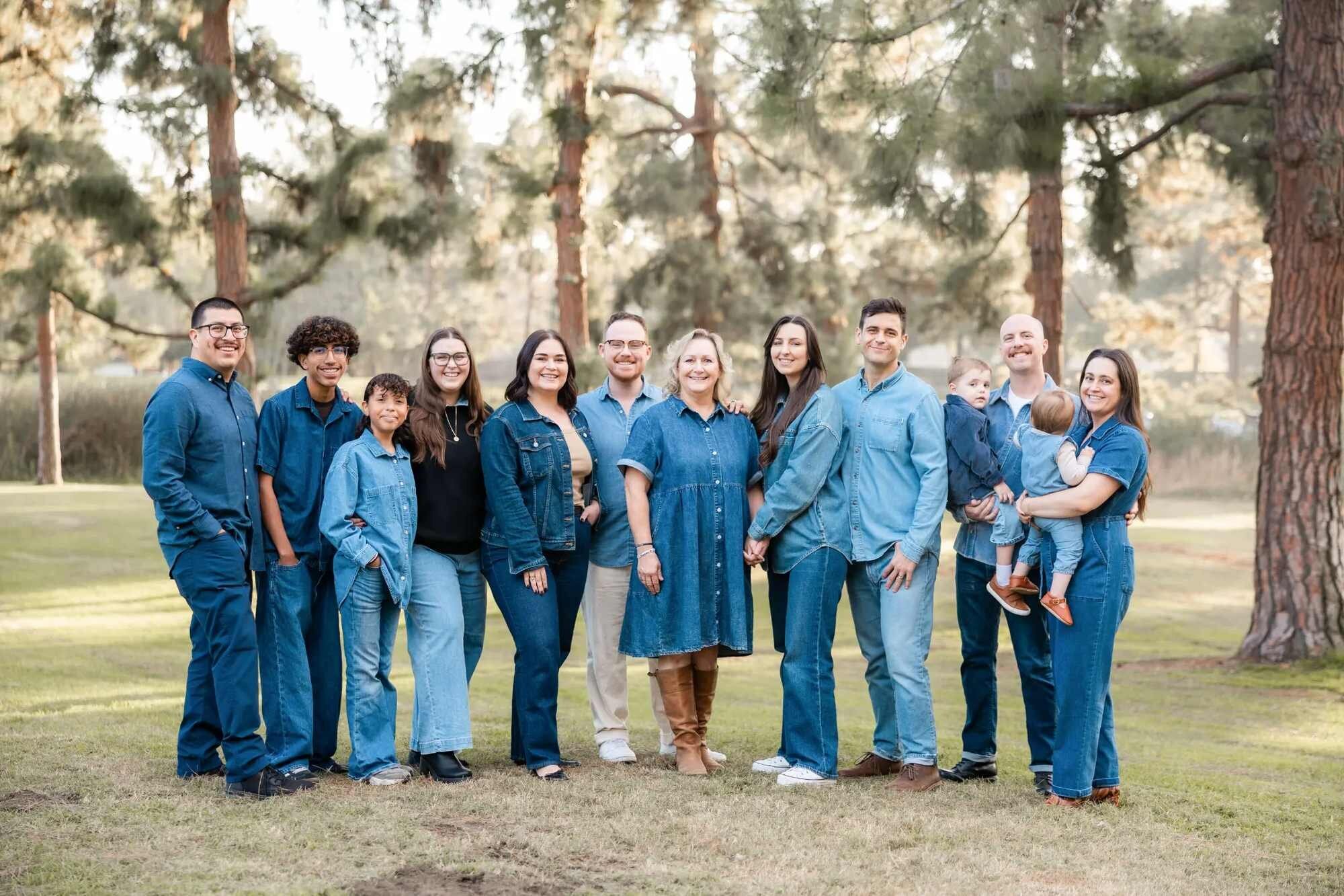Los Angeles family photographer capturing a large multigenerational extended family of eleven smiling together in coordinating denim outfits under tall pine trees at Lake Balboa Park