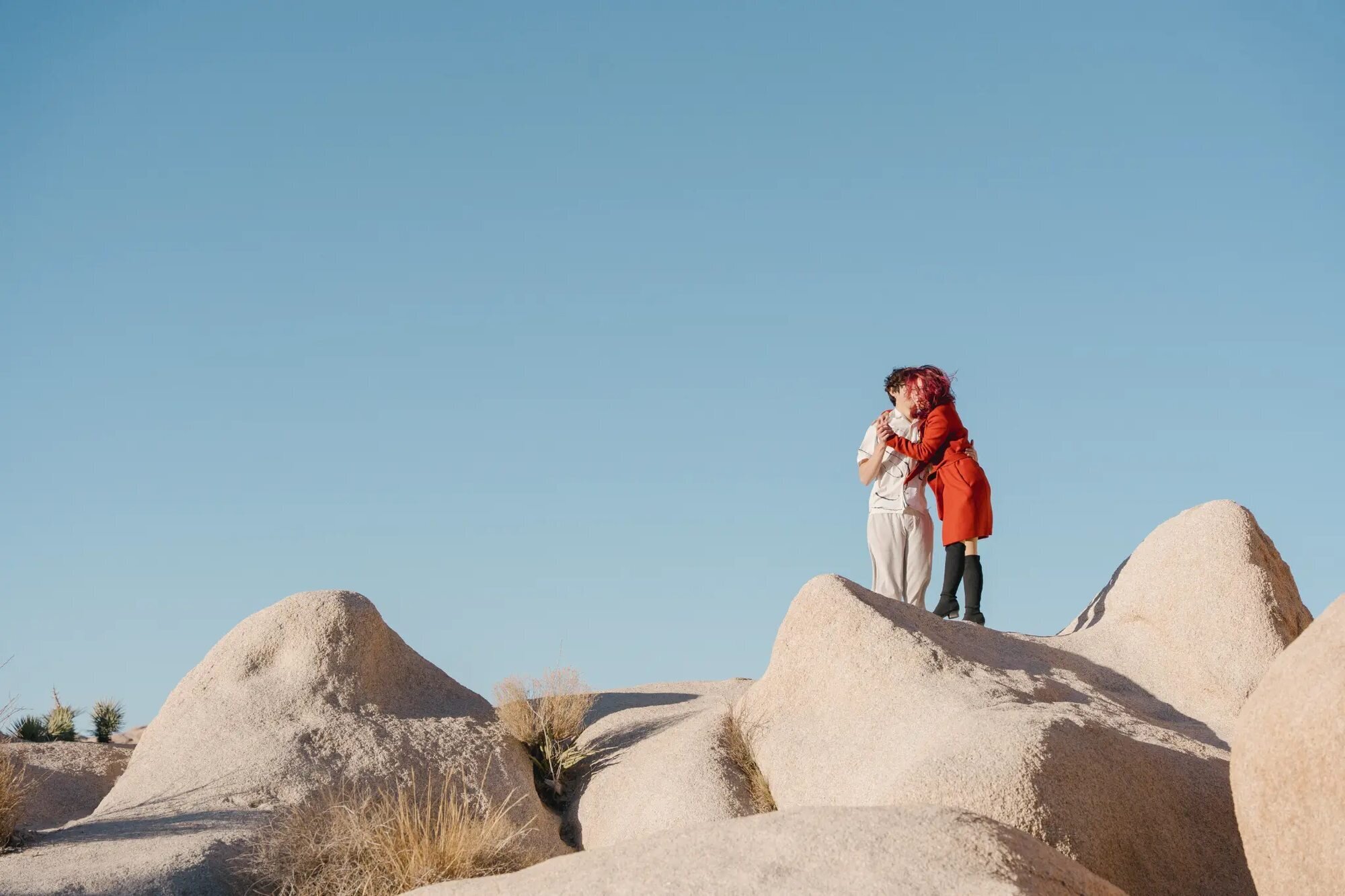 Los Angeles couples photographer capturing a couple embracing on top of large desert boulders at Joshua Tree National Park against a clear blue sky