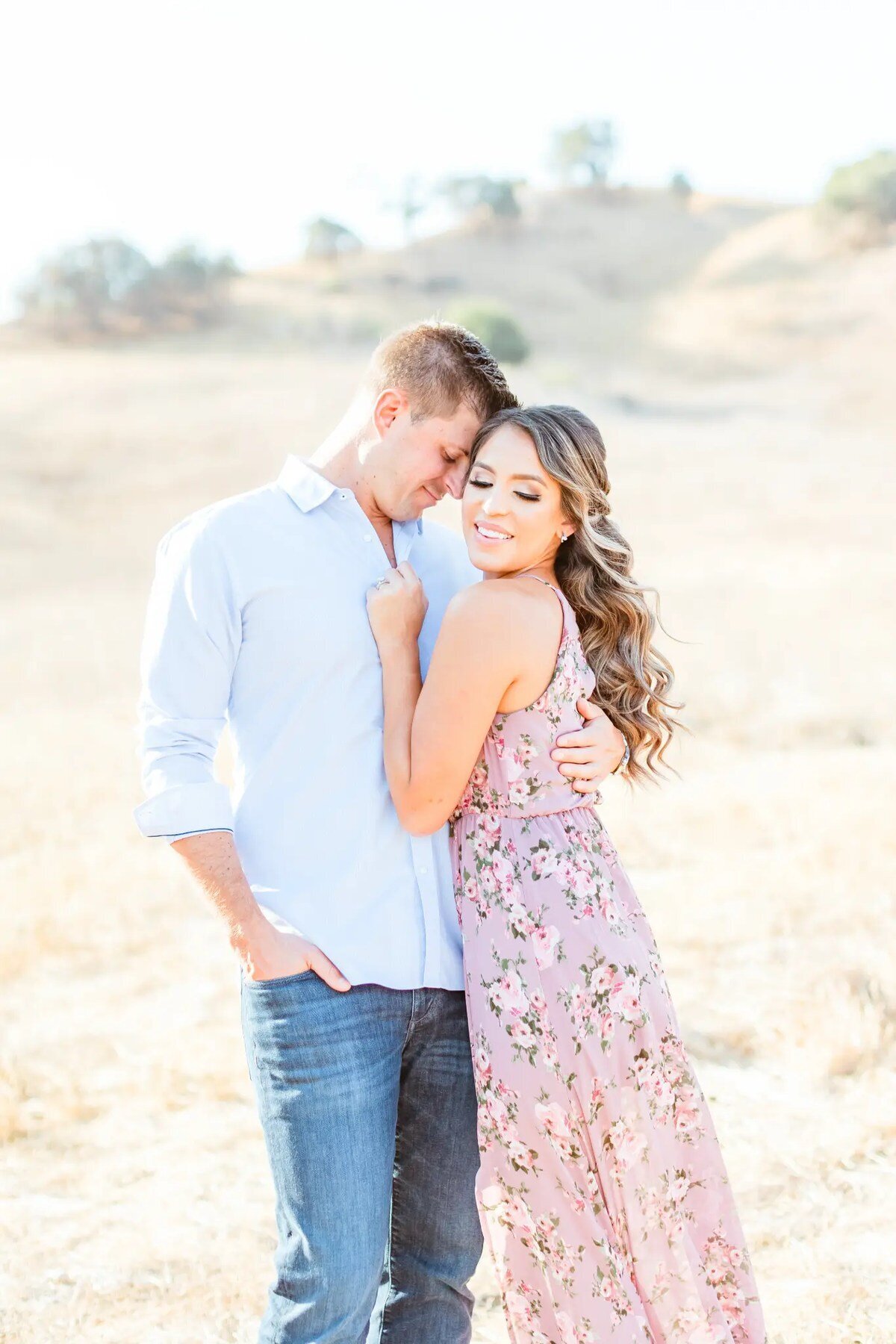 Los Angeles Photographer — Engagement Session at Malibu Creek State Park Los Angeles photographer capturing an engaged couple embracing in a golden dry grass field at Malibu Creek State Park, with the woman in a floral maxi dress smiling at the camera