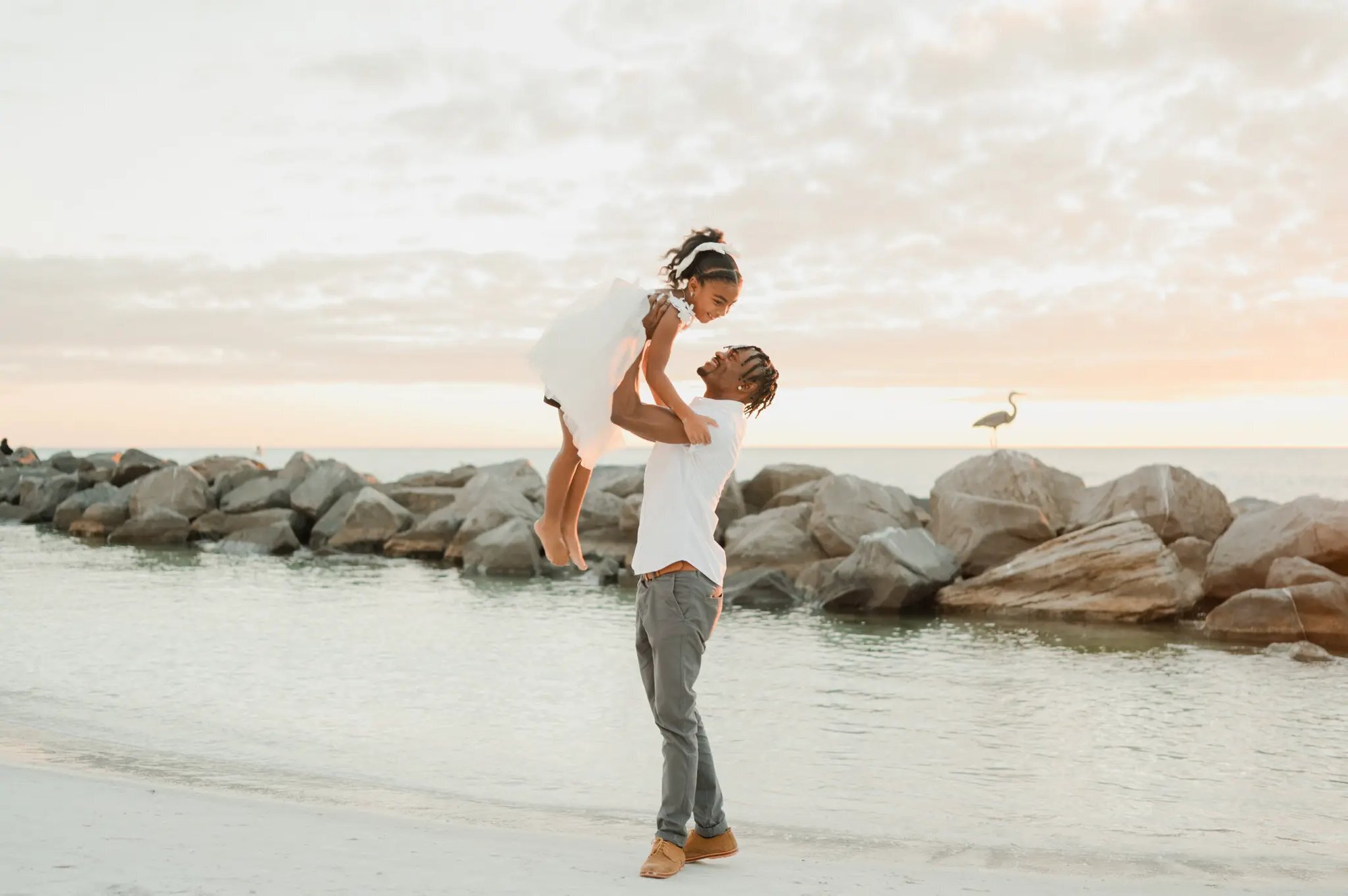 Orlando family photographer capturing a father lifting his young daughter on a Florida beach at sunset with rocky shoreline in the background