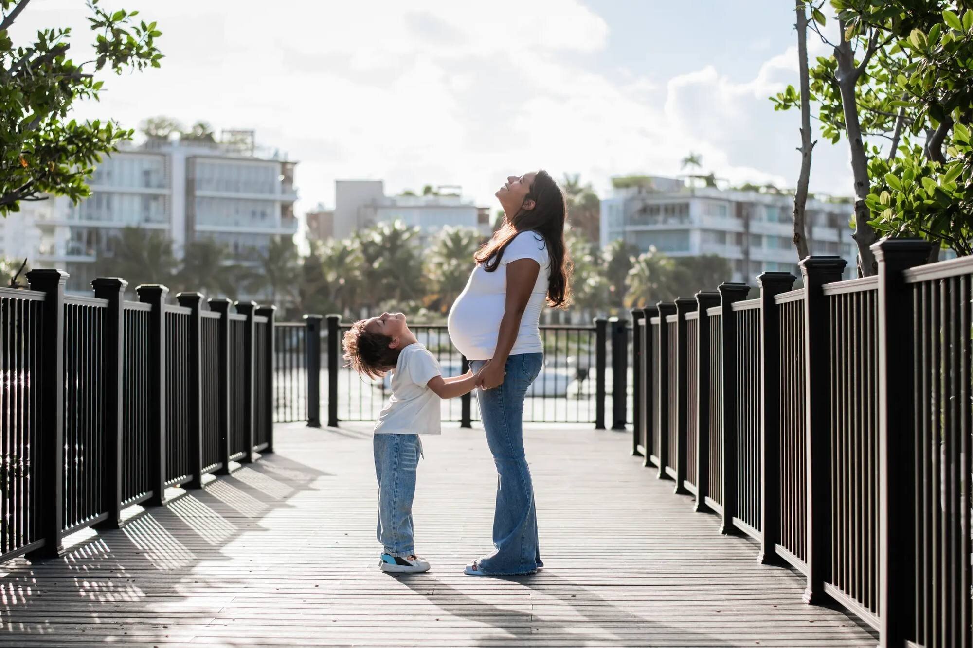 A pregnant woman and her young son standing on the boardwalk at South Pointe Park, Miami, both looking up joyfully — captured by a Dreamgraphy Miami maternity photographer