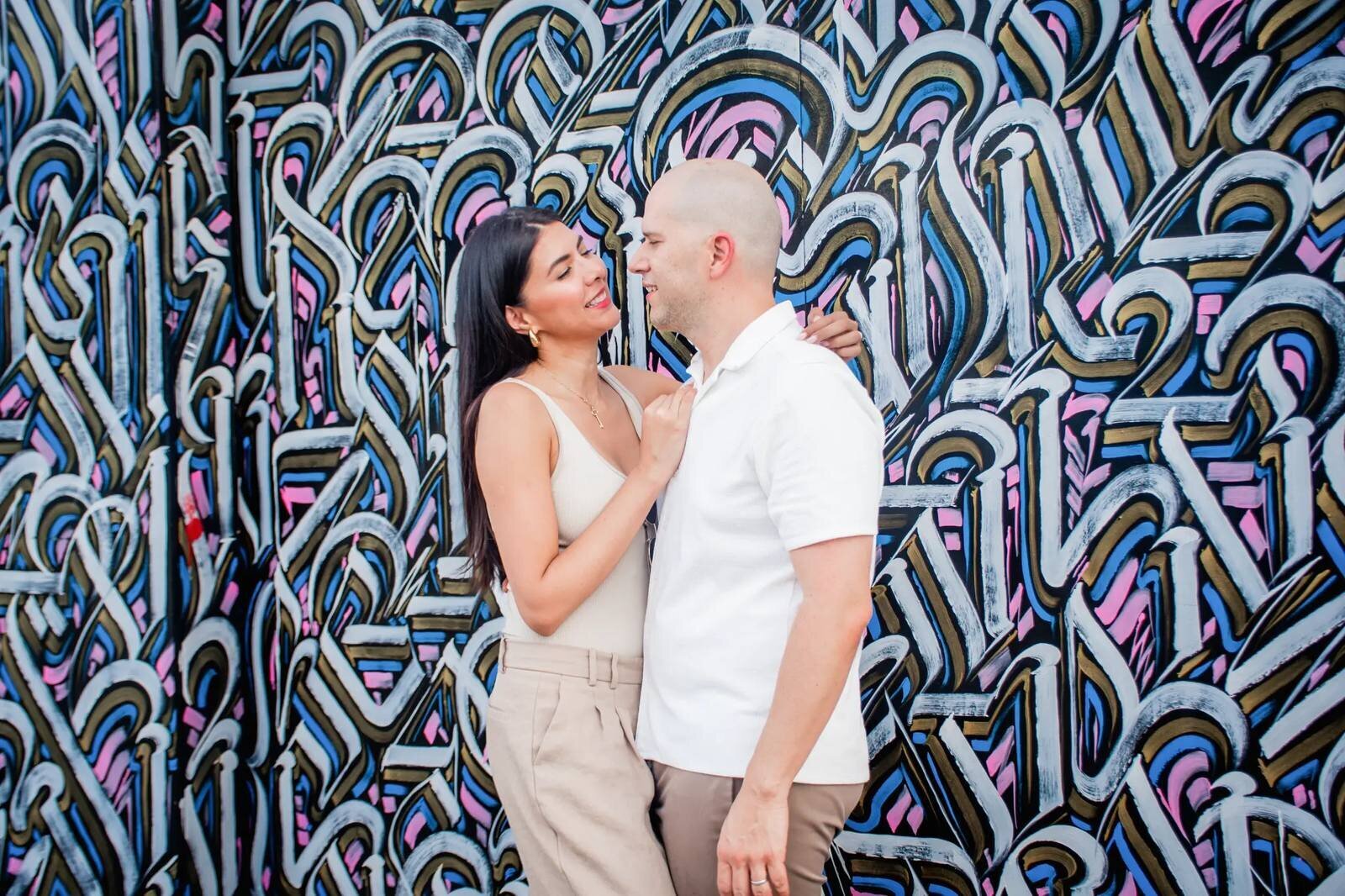 A couple gazing at each other and laughing in front of a vibrant graffiti mural in Wynwood, Miami — captured by a Dreamgraphy Miami couple photographer