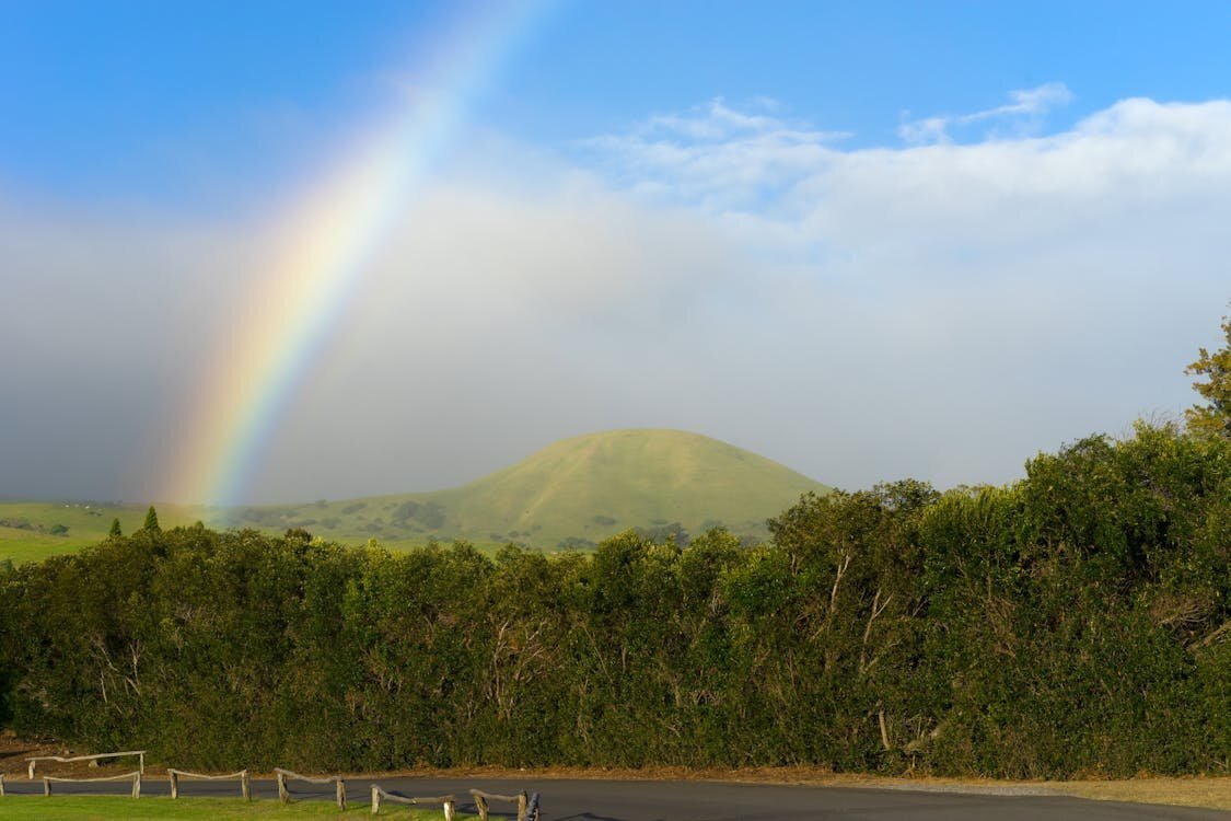 Rolling green hills and lush landscape in Waimea on the Big Island of Hawaii with a rainbow arching over the valley