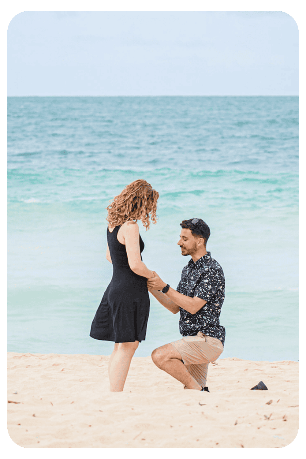 Man proposing to his partner on a beach during a surprise engagement photoshoot captured by Dreamgraphy