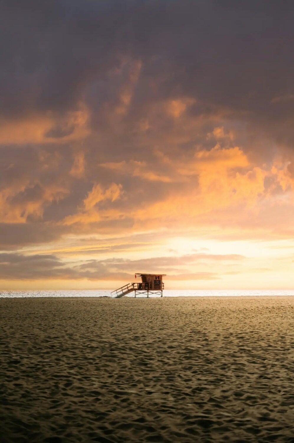 Los Angeles Photographer — Photo Sessions at Crystal Cove State Beach A lifeguard tower silhouetted against a dramatic golden sunset sky on the sandy shores of Crystal Cove State Beach near Los Angeles