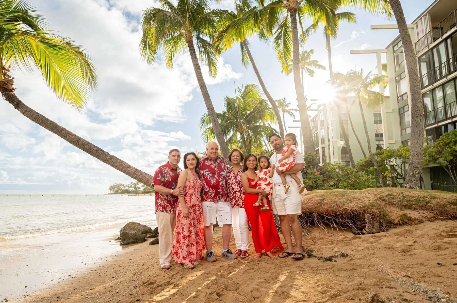 Oahu Family Photos — Extended Family Beach Session with Palm Trees An extended family of eight posing together at Waialae Beach on Oahu with tall palm trees, golden sunlight, and the ocean behind them