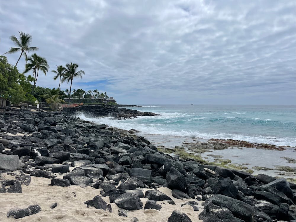 Rocky lava coastline and turquoise ocean at Kailua-Kona on the Big Island of Hawaii with palm trees in the background