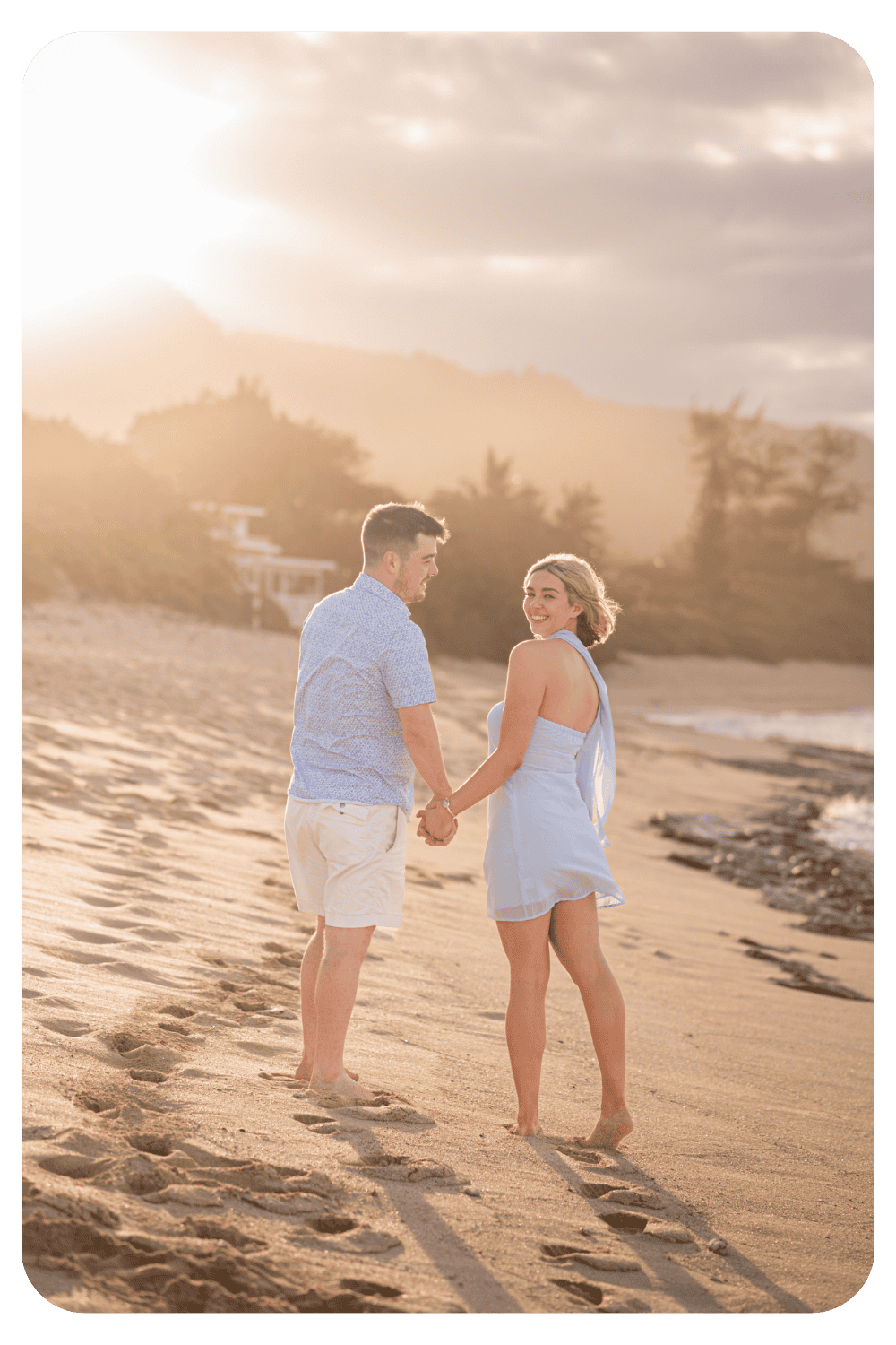 Couple holding hands and walking along a beach at sunset during a romantic vacation photoshoot with Dreamgraphy
