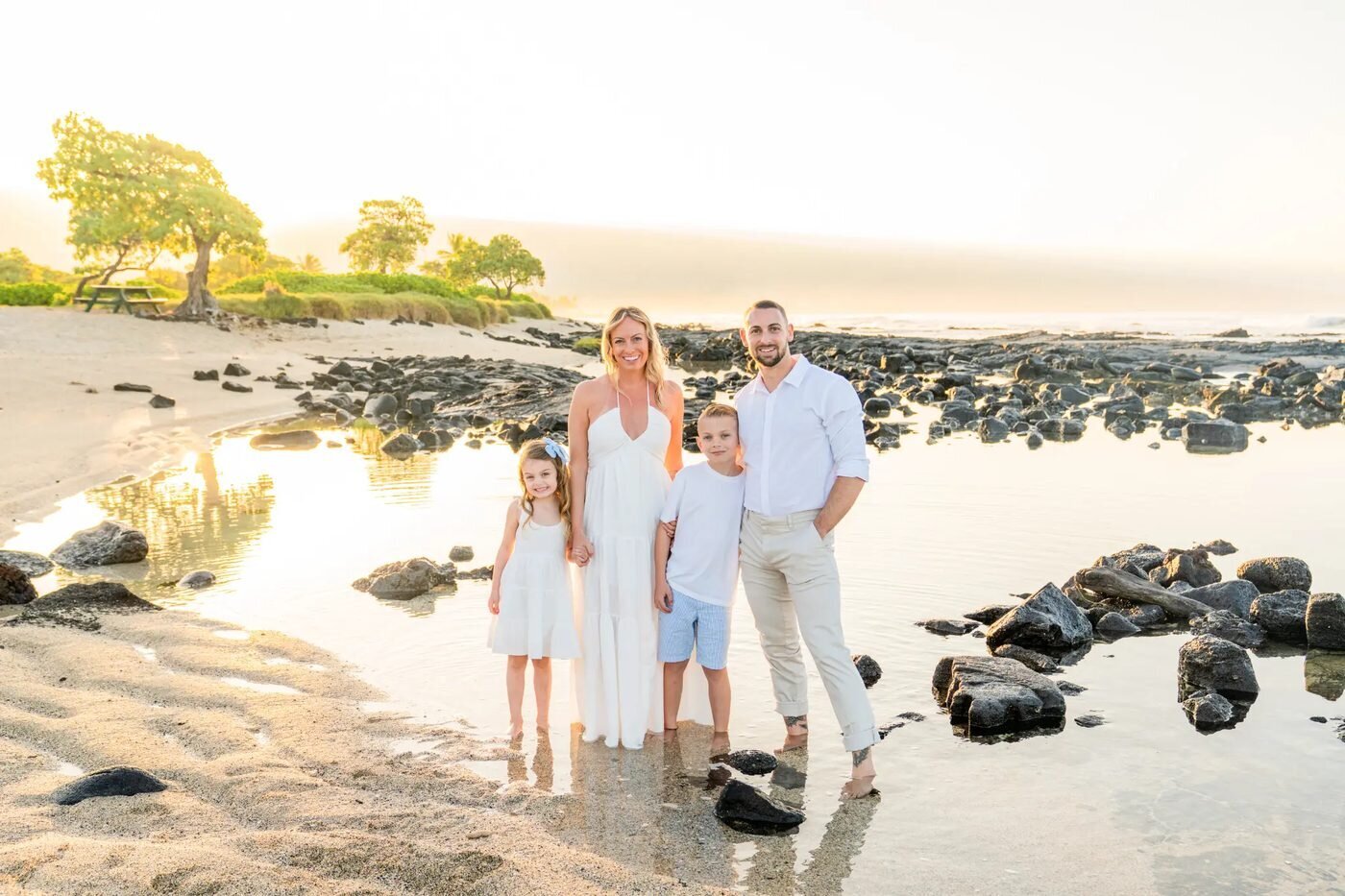 A family of four posing together on a Big Island beach during golden hour with lava rocks and warm sunset light behind them