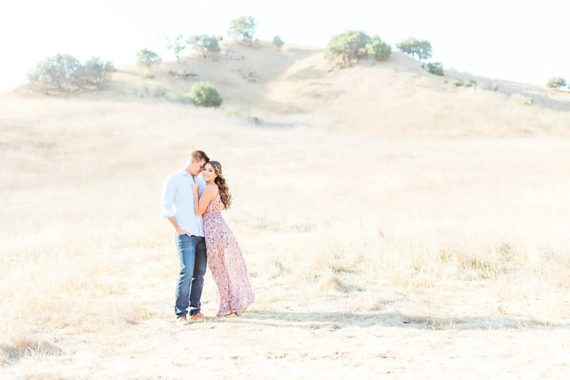 An engaged couple embracing in the golden hills of Malibu Creek State Park during a Los Angeles engagement photography session by Dreamgraphy
