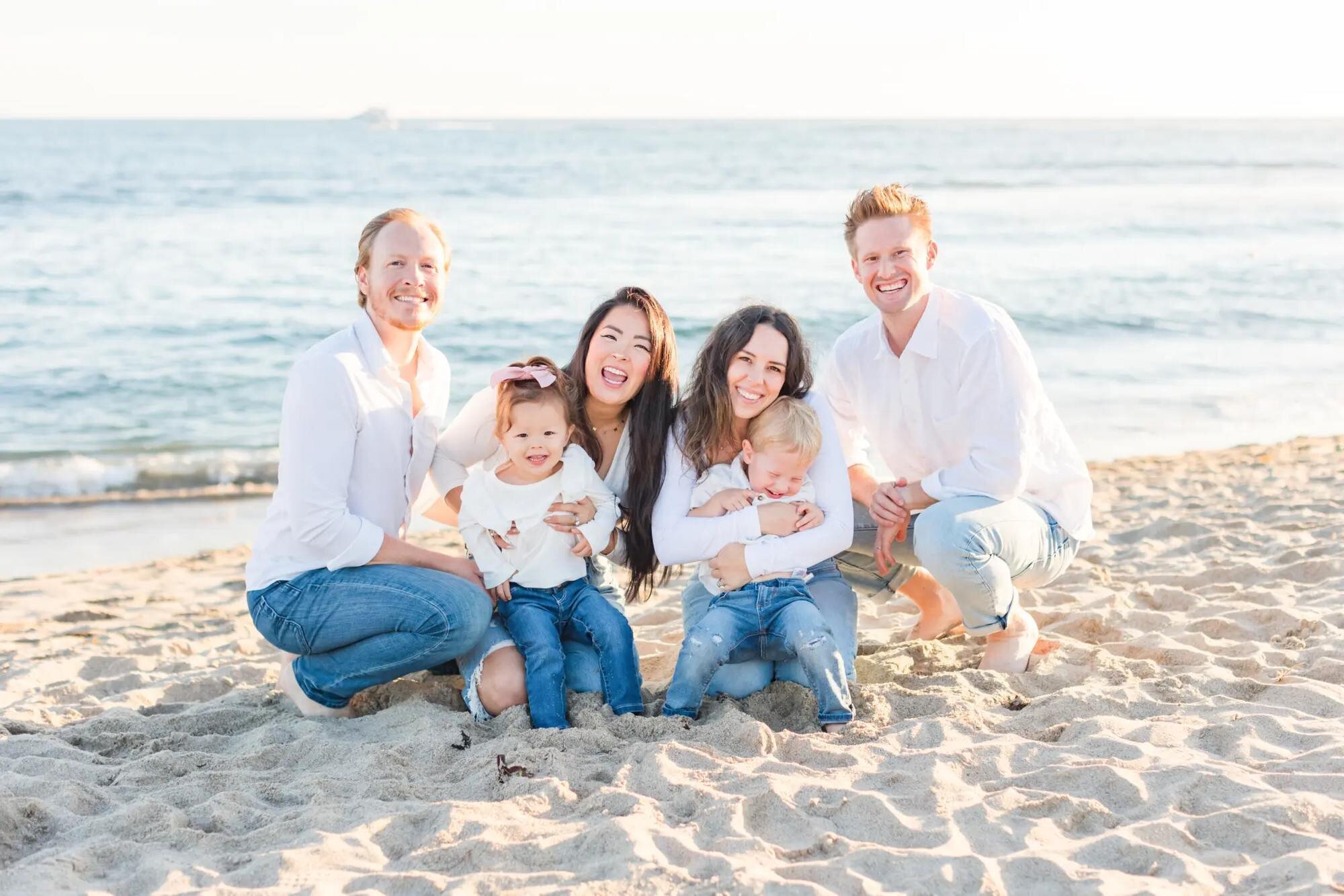 Los Angeles family photographer capturing two young families with toddlers and a newborn laughing together on the sand at Santa Monica Beach at golden hour
