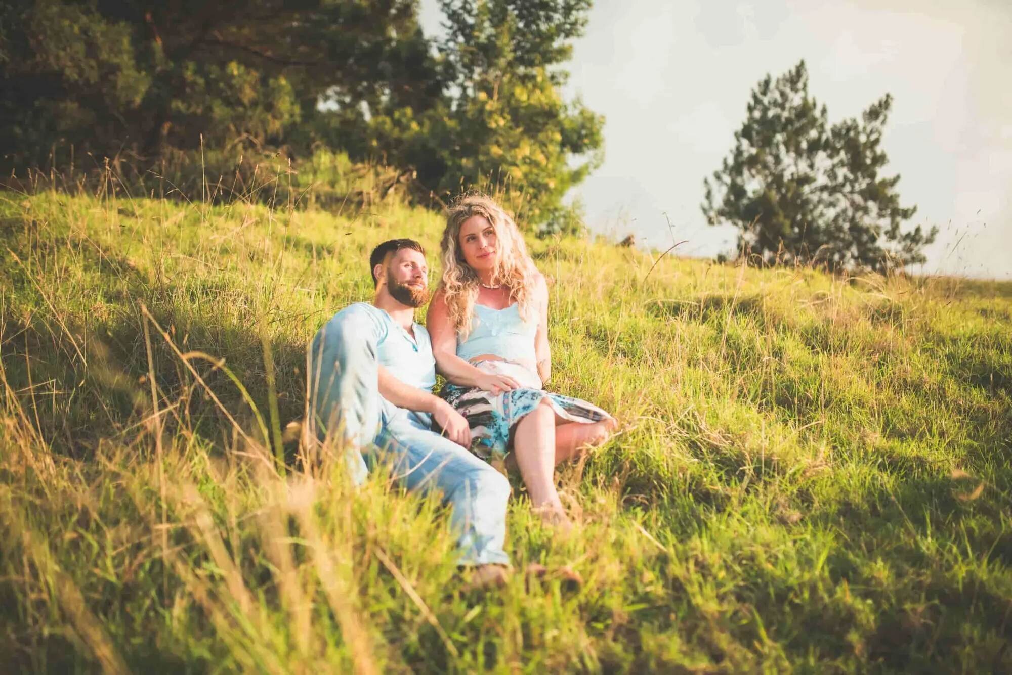 Couple sitting together in a sunlit Upcountry Maui meadow during a romantic engagement session with Dreamgraphy