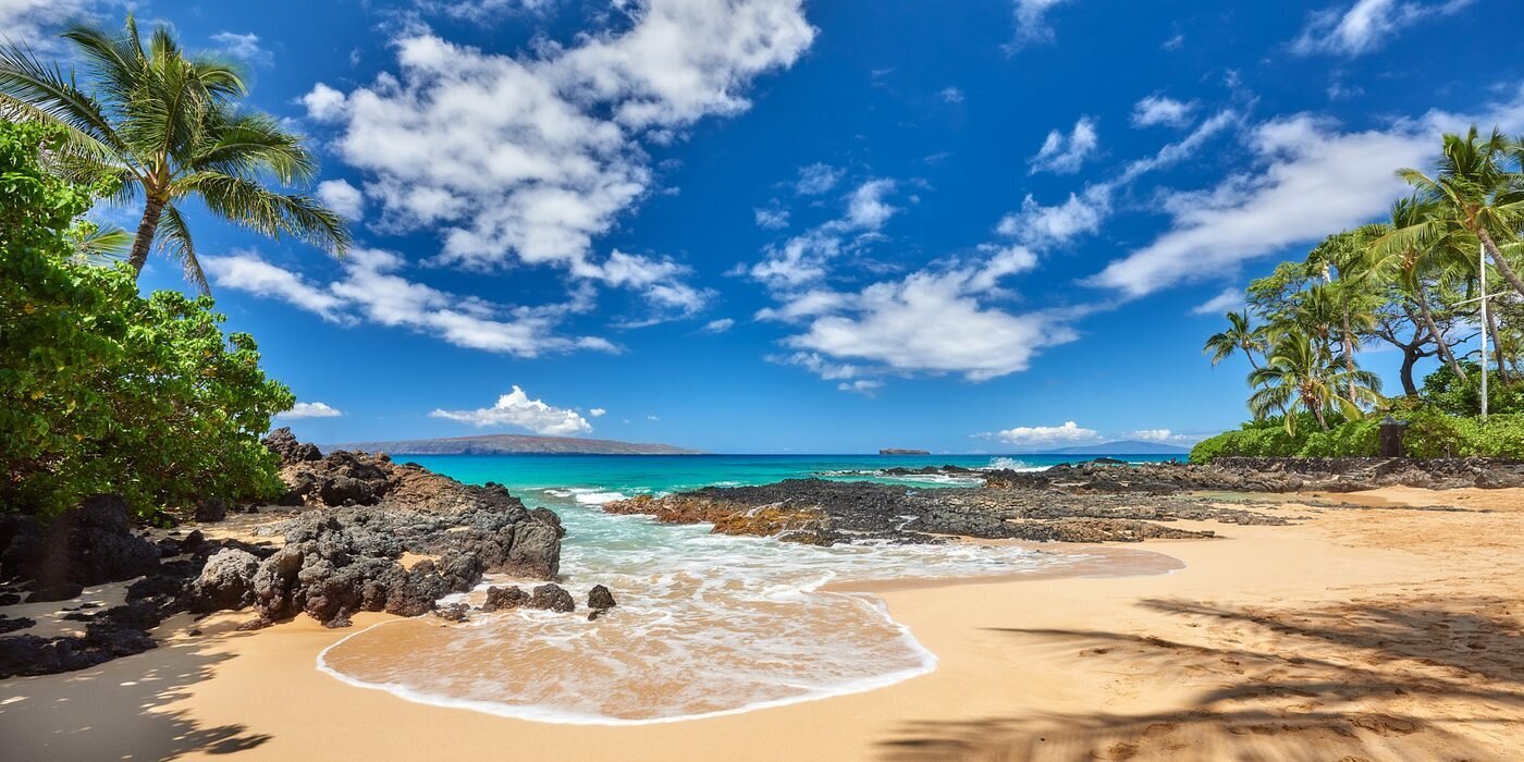 makena-cove-secret-beach-maui-photographer A small golden-sand cove with black lava rocks, palm trees and turquoise water under a bright blue sky at Makena Cove (Secret Beach) on Maui