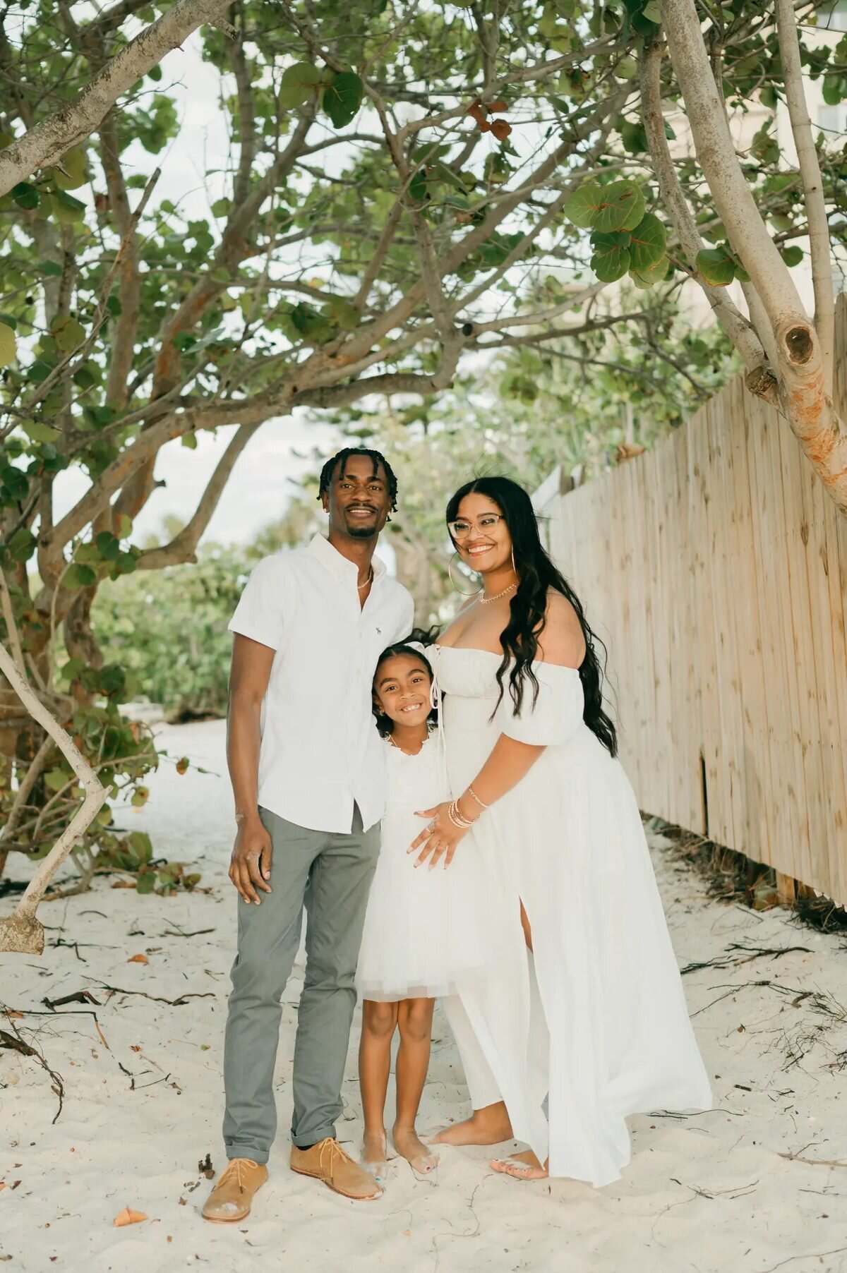 A family of three posing under a canopy of sea grape trees on a sandy path, captured by a professional Orlando family photographer