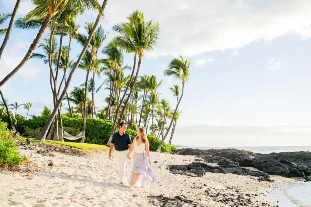 Newly engaged couple walking along the white sand and lava rocks at ʻAnaehoʻomalu Bay on the Big Island of Hawaii