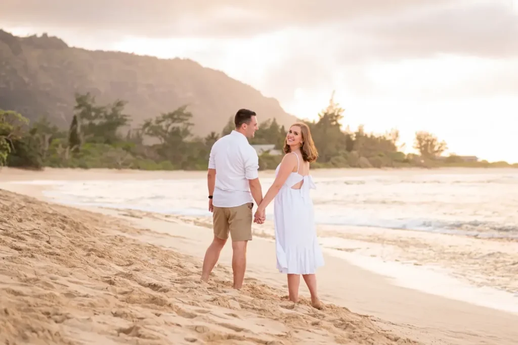 Newly engaged couple walking at Mākua Beach Oahu at golden hour, captured by a proposal photographer