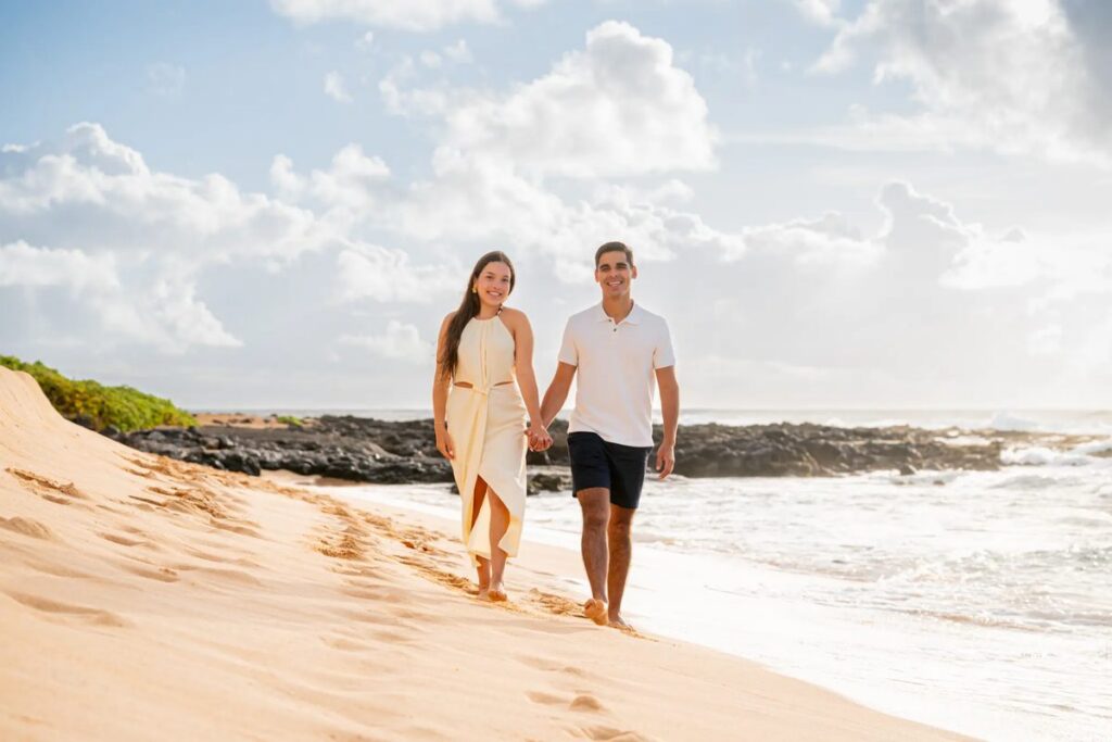A newly engaged couple walking hand-in-hand along a beautiful Maui beach at sunset.